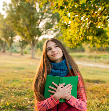 Happy young teenager with book in the autumn park