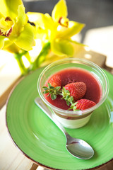 Panacota with strawberries in a cup on a wooden background with flowers