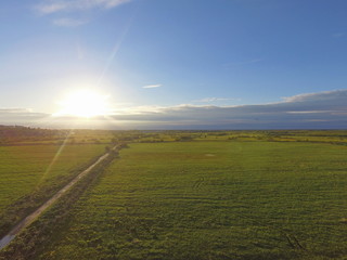 View of the evening sun on the horizon, which illuminates a green field with rural road. Vylgort