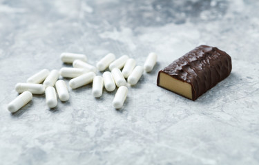 High Protein bar and Arginine capsules.  Bodybuilding food supplements on bright stone background. Close up. Copy space. 
