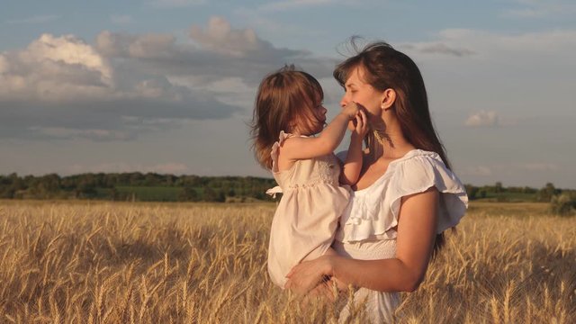 mother walks with the baby in the field hold spikelets with wheat in hand. little daughter kisses mom on wheat field. happy family travels. baby in the arms of mom. happy family concept.