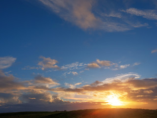 Fototapeta na wymiar Cloudy sunset sky over a hill silhouette. Blue and orange color, Soft warm sun glow.