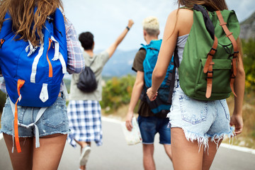 Group of young people with backpacks walking together by the road