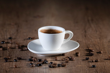 Top view of a white coffee cup surrounded by coffee seeds on a wooden table