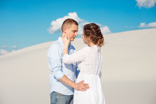 Young man and woman hugging on a background of white sand, dunes. Love story in the void