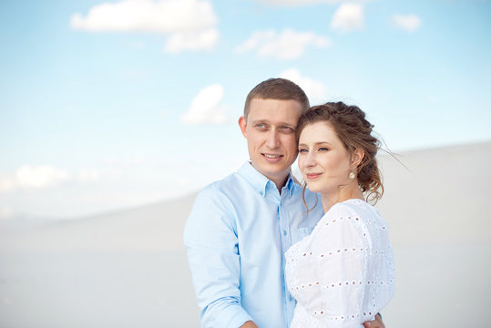 Young man and woman hugging on a background of white sand, dunes. Love story in the void