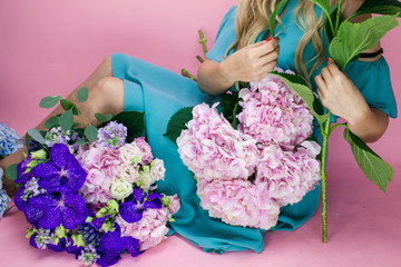 Female florist create a bouquet at workplace. Floristics workshop. Making beautiful flower bouquets and floral decorations. Young woman with flowers on the isolated background. 