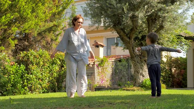 Little boy having fun while visiting grandmother. Healthy lifestyle concept. Happy childhood concept. Cheerful boy jumping with young grandmother on backyard. Summer vacations, holidays