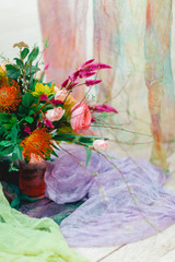 Beautiful multi-colored bouquet in a white room on a background of colorful fabrics