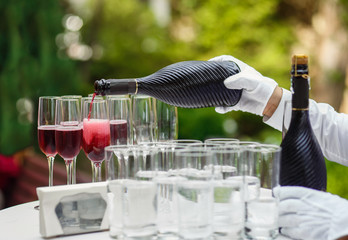 The waiter pours sparkling red wine into glass goblets. Outdoor party with alcohol. Waiter's hand...