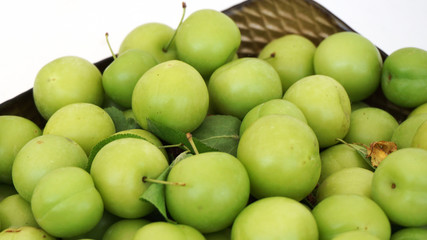 green plums on white ground, fresh plums, sour plums in a container, green and sour plums,