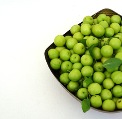 green plums on white ground, fresh plums, sour plums in a container, green and sour plums,