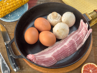 Eco chicken eggs.Champignons.Bacon of pork belly are fried in a black cast iron skillet.On wooden background 