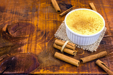 Fototapeta na wymiar Dessert of curau. Brazilian sweet corn, corn mousse with cinnamon on a wooden background. Typical Brazilian dessert, sweet of June party. Dessert, canjica or Jimbelê.