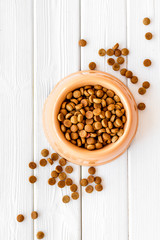 Cat dry food in bowl on white wooden background top view mock up