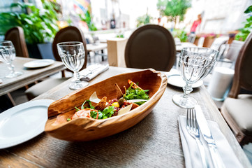 view from restaurant table served with glasses,  cutlery and wooden bowl of vegetable appetizer on summer terrace 
