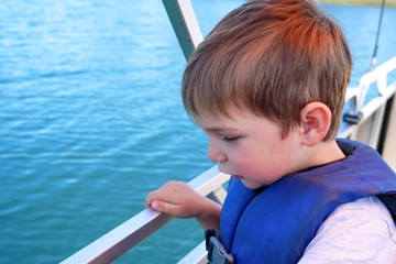 Cute little boy enjoying ride on a small boat. Little kid in the bow of a boat with his blue life jacket having fun. Travel adventure family vacation.