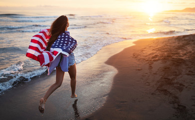 Cheerful happy woman outdoors on the beach holding USA flag having fun.