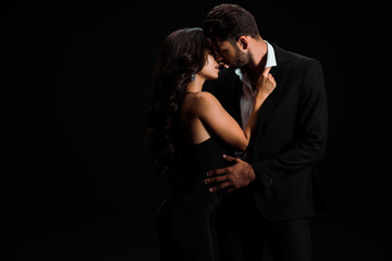 attractive girl touching suit of passionate bearded man isolated on black
