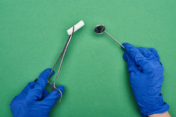 cropped view of dentist in blue latex gloves holding scissors with cotton pad and medical mirror on green