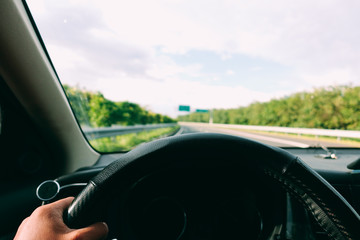 Inside view, hand of a driver on steering wheel of a car with empty asphalt road background. High-quality free stock image of driver hands on the steering wheel inside. Summer trip or vacation by car