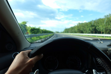 Inside view, hand of a driver on steering wheel of a car with empty asphalt road background. High-quality free stock image of driver hands on the steering wheel inside. Summer trip or vacation by car