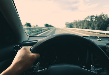 Inside view, hand of a driver on steering wheel of a car with empty asphalt road background. High-quality free stock image of driver hands on the steering wheel inside. Summer trip or vacation by car