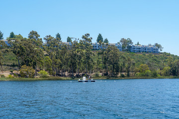 Fototapeta na wymiar Big lake with blue water, trees and native wetland plants and villa on the cliff with blue sky. Miramar reservoir in the Scripps Miramar Ranch community, San Diego, California