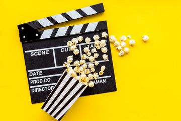 Go to the cinema with popcorn and clapperboard on yellow background top view