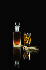 Obraz premium a glass of iced whisky and a bottle of whisky with wheat on reflected floor on dark background