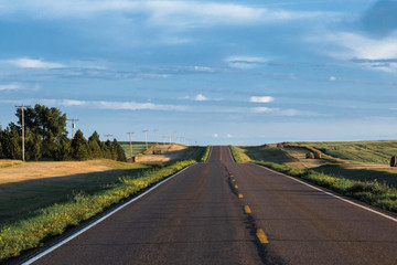 a long remote highway in rural North Dakota with a bright blue sky with clouds in the horizon