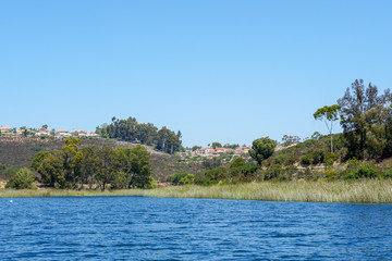 Big lake with blue water, trees and native wetland plants and villa on the cliff with blue sky. Miramar reservoir in the Scripps Miramar Ranch community, San Diego, California
