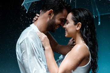 side view of positive bearded man hugging cheerful girl and holding umbrella on black