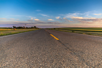 a long remote highway in rural North Dakota with a bright blue sky with clouds in the horizon - obrazy, fototapety, plakaty