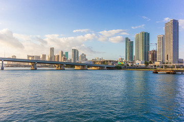 Fototapeta na wymiar Miami city skyline panorama at blue sky cloudy with urban skyscrapers and bridge over sea with reflection