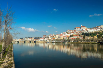 Fototapeta na wymiar Cityscape of Coimbra in Portugal with the Mondego river in the foreground and the reflection of the city in its waters on a sunny winter morning.