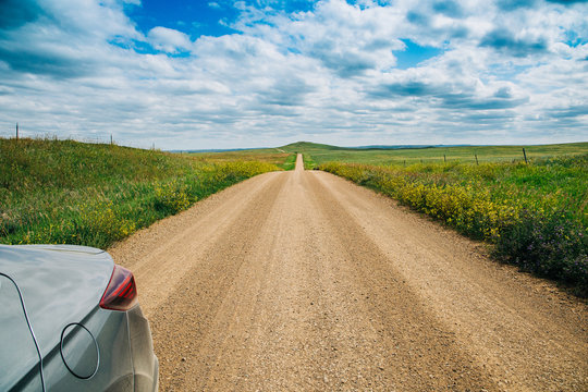 The Side Of A Car On A Long Dirt Road In Rural North Dakota With A Bright Blue Sky With Clouds In The Horizon