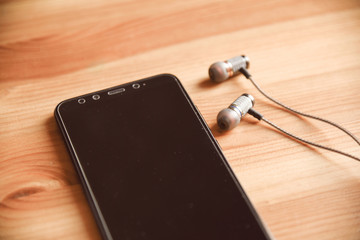 Black headphones and smartphone lies on wooden background. Design layout, smart phone with black screen and wired headphones with copy space.