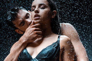 low angle view of shirtless and wet man touching face of attractive girlfriend with closed eyes...