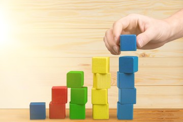 Hand with toy wooden blocks stack, towers of blank multicolor box cubes over white background