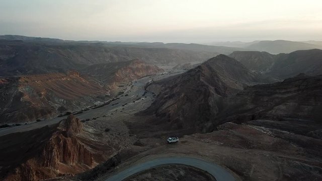 Flying over large cliff in the desert with lonely van Drone footage over High clif and desert rocky mountains with single van
