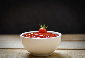 Fresh tomatoes on ketchup in cup tomato sauce on wooden and black background