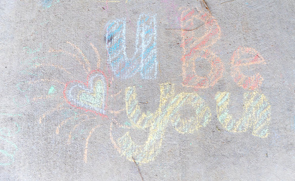the words "U Be You" written with sidewalk chalk on gray concrete pavement background