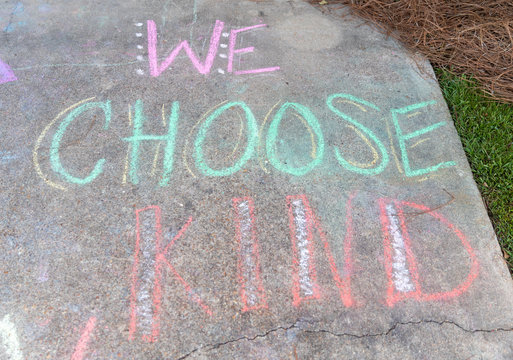 the words "We Choose Kind" written with sidewalk chalk on gray concrete pavement background