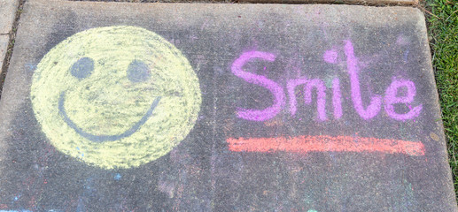 the word "Smile" written with sidewalk chalk on gray concrete pavement background