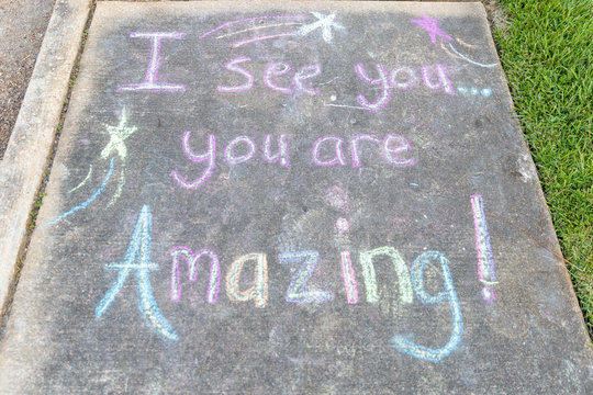 the words "I See You, You are Amazing" written with sidewalk chalk on gray concrete pavement background