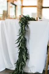 Garland of greenery on table at wedding reception, white table cloth, minimal and modern wedding flowers