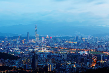 Sunset scenery of Downtown Taipei, vibrant capital city of Taiwan, with landmark  tower standing out amid high-rise buildings in Xinyi Financial District & colorful city lights dazzling in twilight