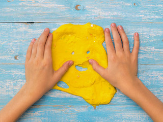 Child smoothes hands yellow slime on a blue table.