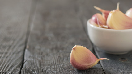 Slices of fresh garlic in a white bowl on a black wooden table. Component of traditional medicine.